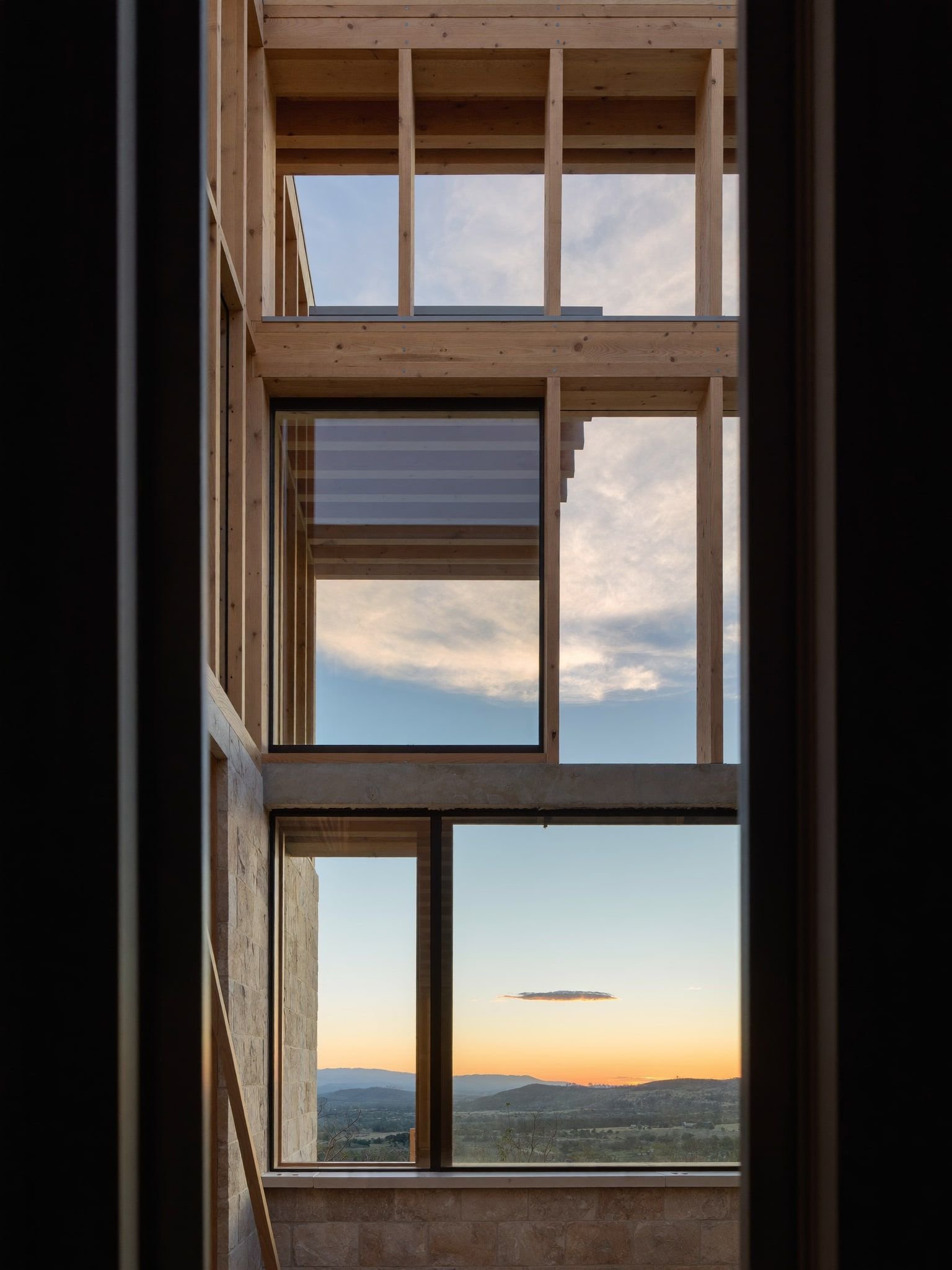Hill Country custom home under construction at sunset, exposed timber framing and limestone around large window openings