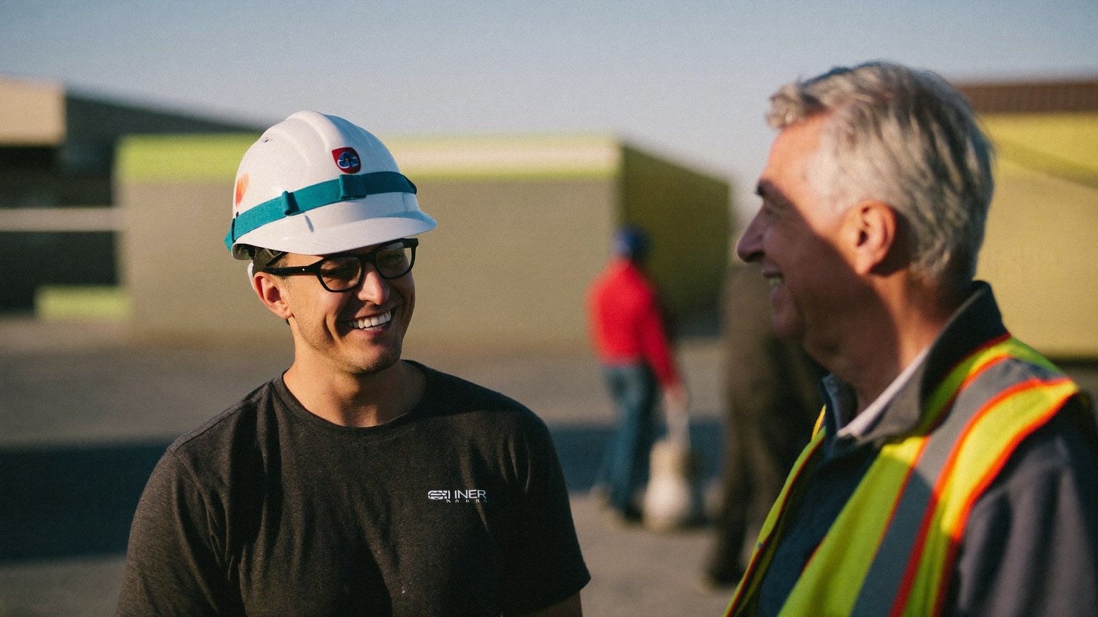 A young field engineer laughing with a senior superintendent on a jobsite in warm afternoon light