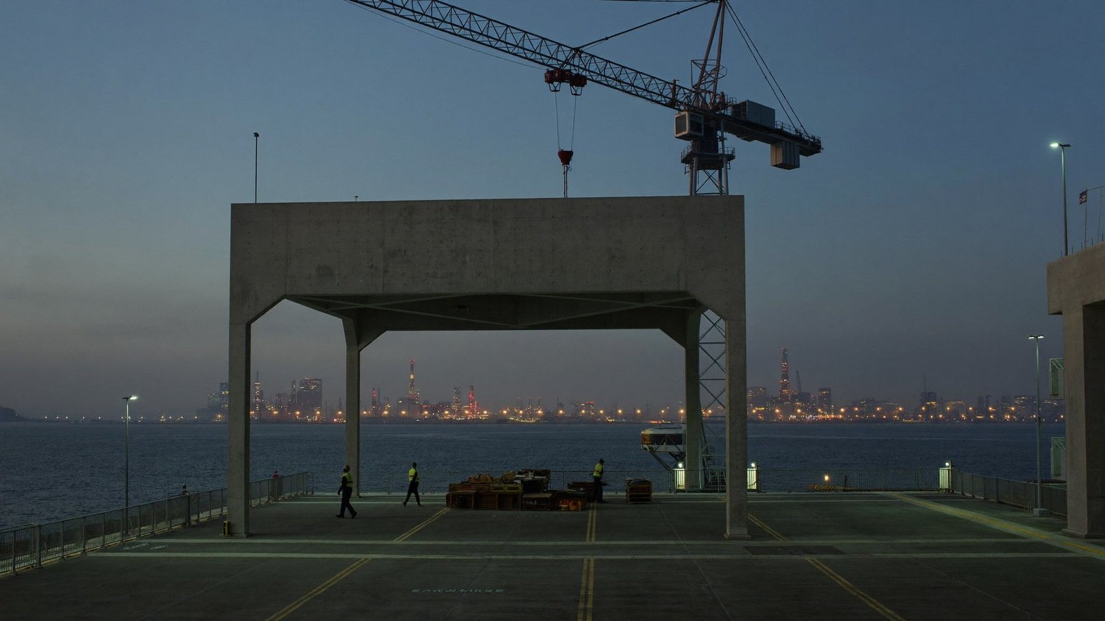 Concrete structure under construction near the Houston Ship Channel at dusk, refinery lights on the horizon