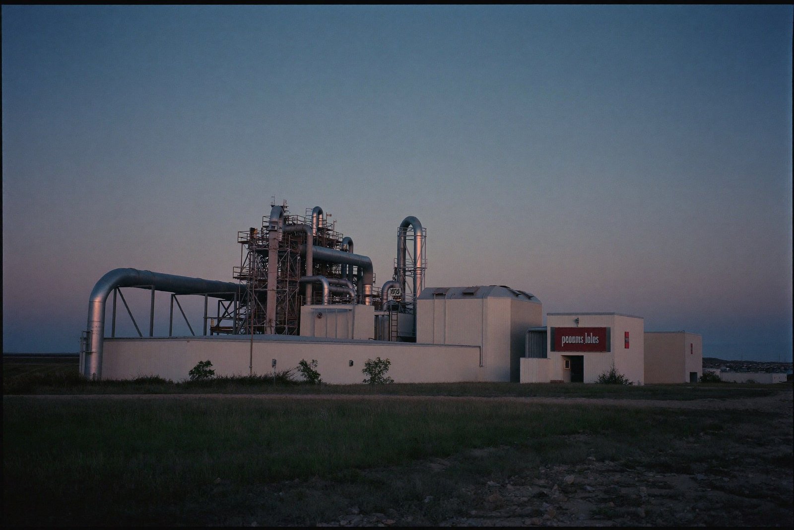 Industrial energy facility at blue hour with steel pipe racks and a low control building