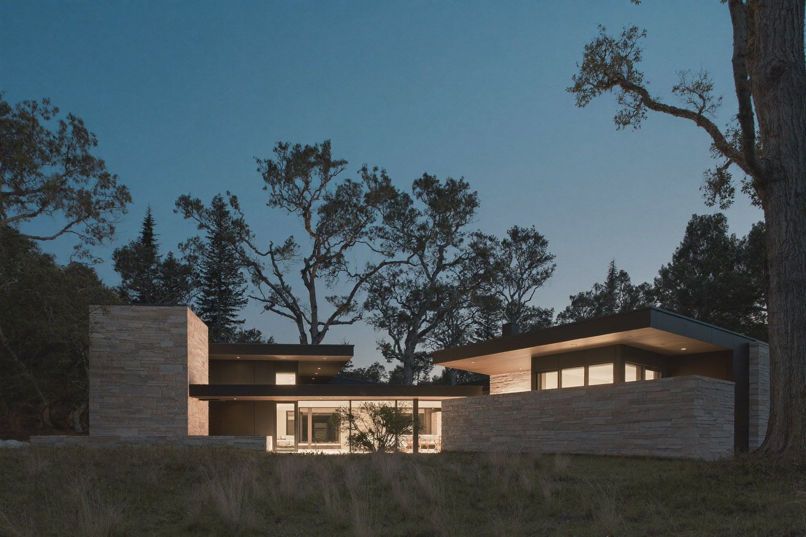 Modern limestone and glass custom home glowing warm at blue hour under live oaks