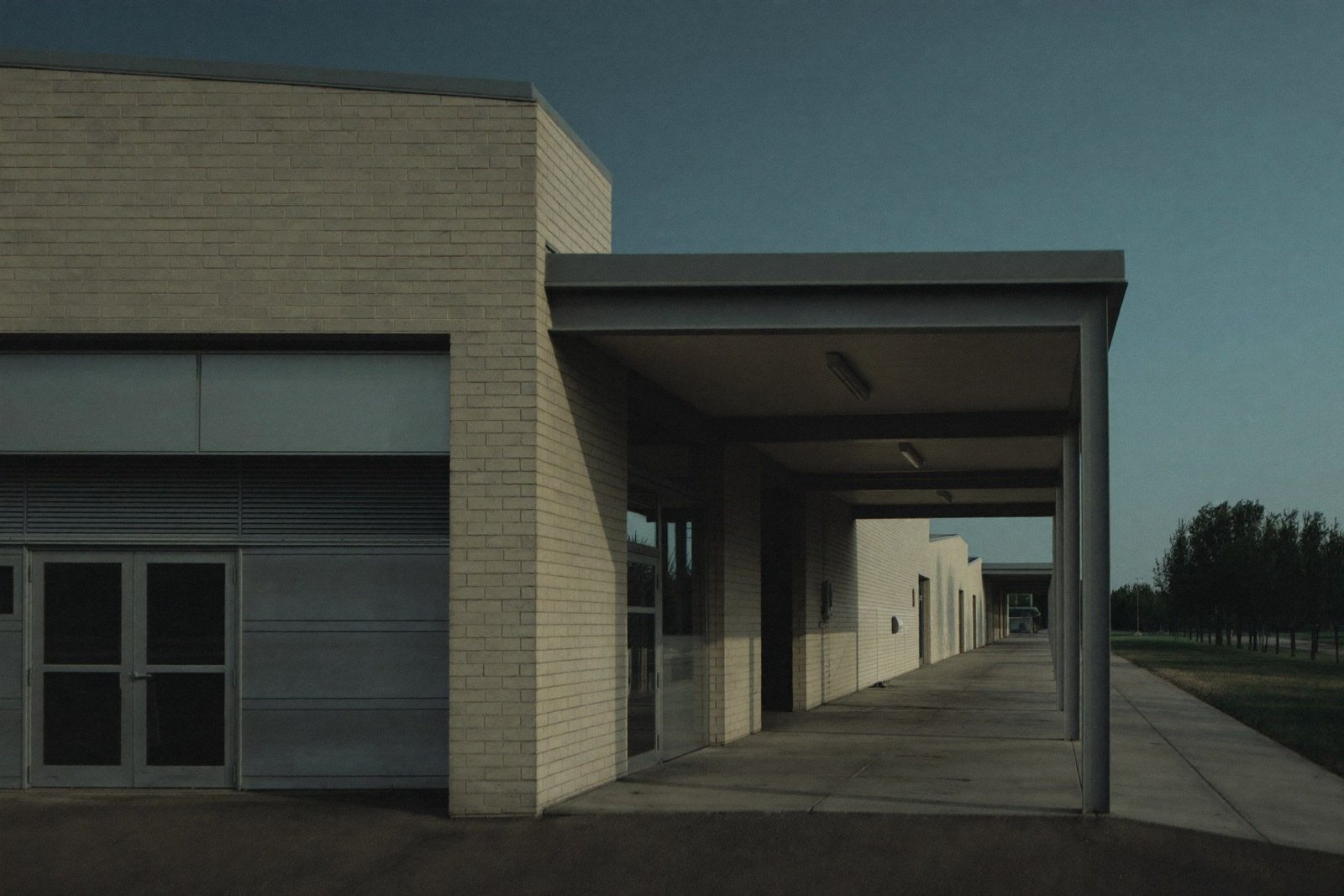 School addition with brick and metal panel facade, covered walkway and bus loop at blue hour