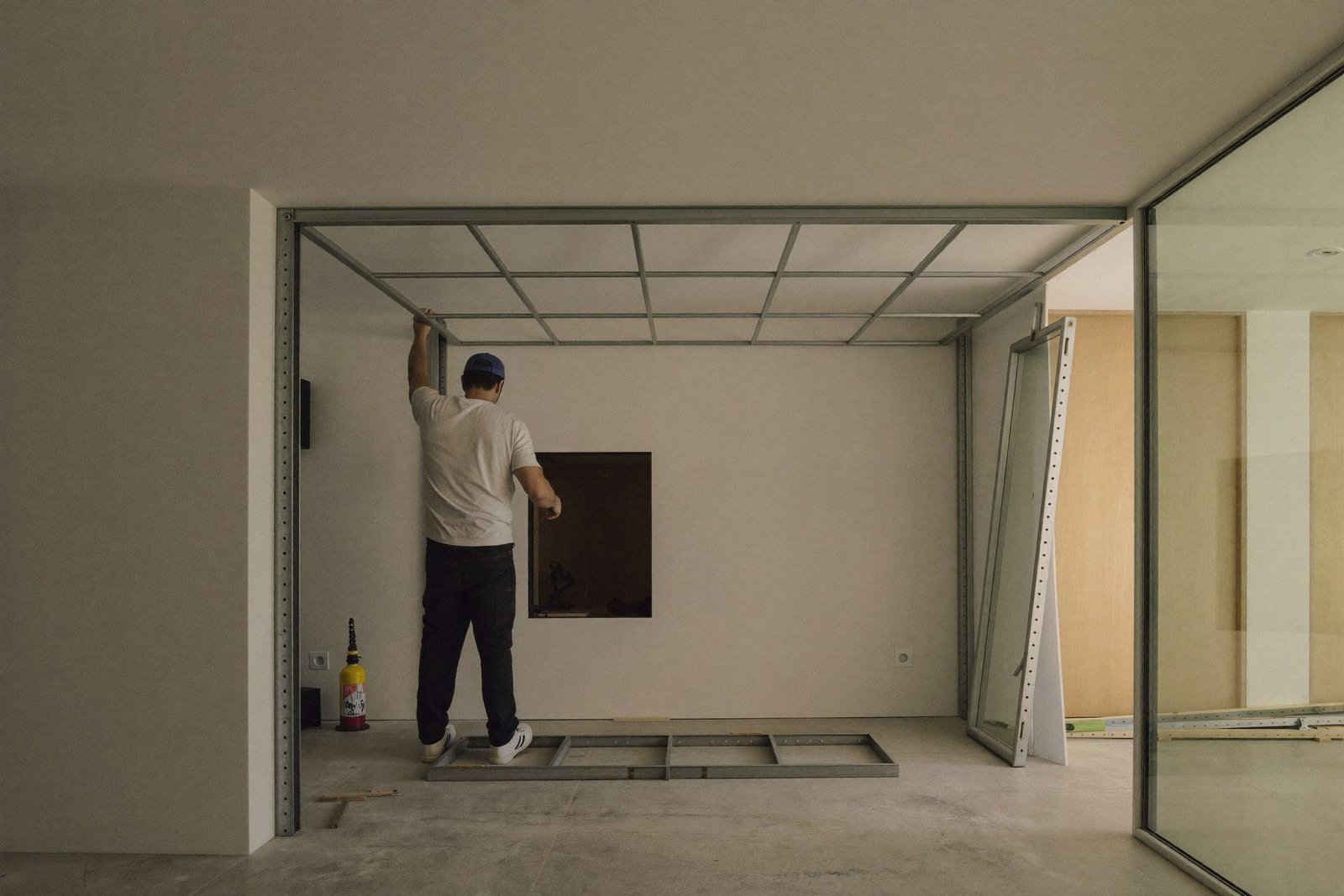 Worker installing ceiling grid in a tenant finish-out with metal stud framing and daylight from a curtain wall