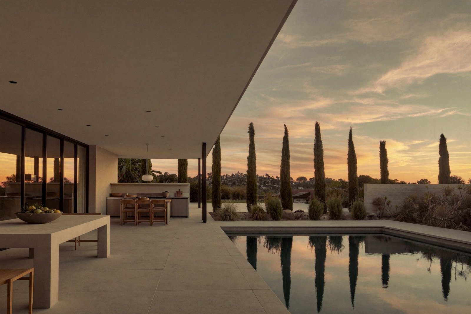 Covered limestone patio with outdoor kitchen and pool at dusk behind a modern Texas home